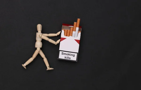 木偶把一包香烟放在黑色背景上 吸烟成瘾 吸烟使人死亡 — 图库照片