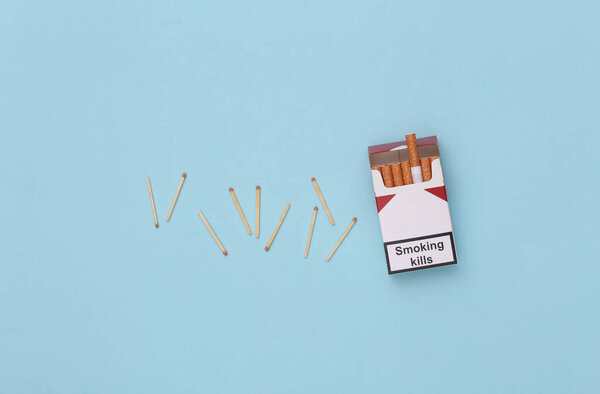 Пачка сигарет и спичек на синем фоне. Вид сверху