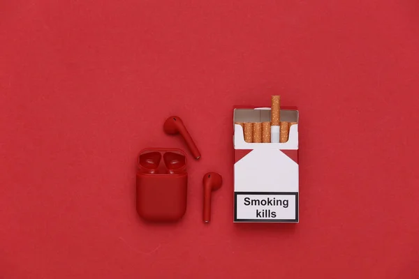 ワイヤレスヘッドフォンと赤い背景にタバコのパック トップ表示 — ストック写真
