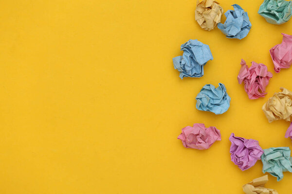 Many colored crumpled balls of paper on yellow background with copy space.