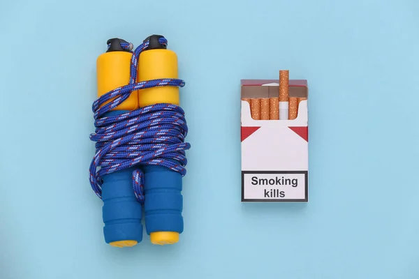 体育或坏习惯的概念 跳绳和一包香烟 蓝色背景 顶部视图 — 图库照片