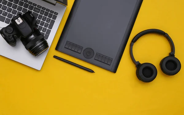 Workspace of photographer or retoucher. Laptop, graphic tablet, camera and headphones on yellow background. Top view.