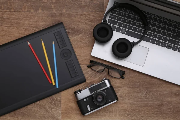 Workspace of a photographer or retoucher. Laptop, graphic tablet, camera and headphones on wooden background. Top view