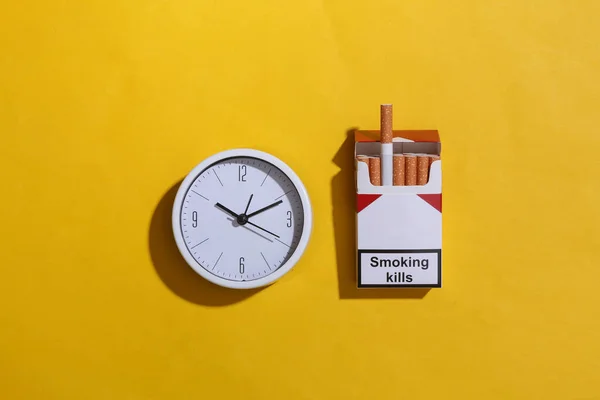 黄色背景上的香烟和时钟包 顶部视图 — 图库照片