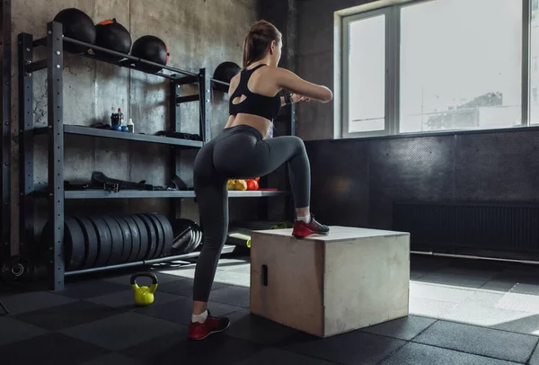 Attractive fit woman doing lunges on wooden box in gym