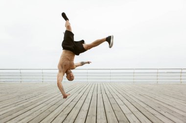 Kaslı bir adam ellerini kumsalda yere değdirmeden baş aşağı zıplıyor.