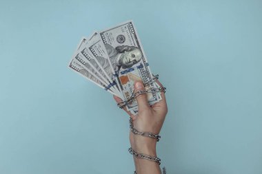 Çelik bir zincire sarılı bir el mavi arka planda sddollar banknotları tutar. Suç kavramı