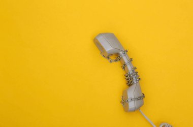 Telefon ahizesi sarı arka planda çelik bir zincire sarılı. Üst görünüm