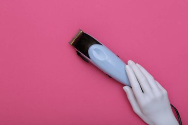 Pembe arka planda saç makası tutan bir mankenin beyaz eli. Güzellik ve moda