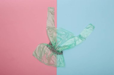 Mavi-pembe pastel arka planda çelik zincire sarılı selofan çanta. Üst görünüm