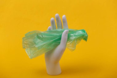 Beyaz manken, sarı arka planda plastik torba tutuyor. Çevre kirliliği. Eko kavramı