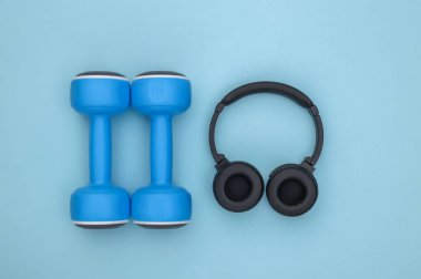 Mavi arka planda dambıllar ve stereo kulaklıklar. Spor konsepti. Üst görünüm