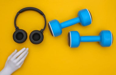 Dambıllar ve stereo kulaklıklar, sarı arka planda manken eli. Spor konsepti. Üst görünüm