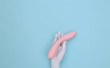 Mavi pastel arka planda beyaz manken kadın seks oyuncağını tutuyor. Üst Manzara. Minimalizm