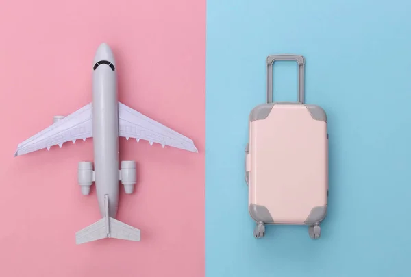 Air travel flat lay. Mini plastic travel suitcase and air plane on pink blue pastel background. Top view.