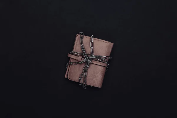 Leather wallet wrapped in a steel chain on black background.