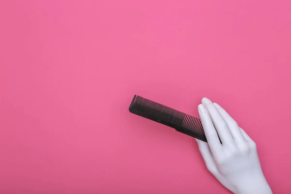 Mannequin hand holding comb on pink background. Minimalism beauty concept