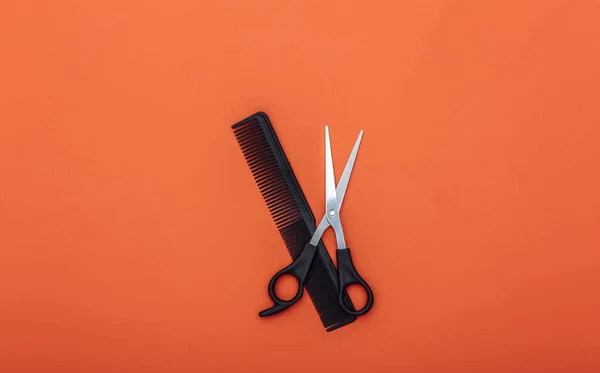 Comb and scissors on orange background. Barber tool. Top view