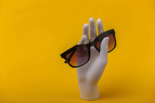 Biała Ręka Manekina Trzymająca Okulary Przeciwsłoneczne Żółtym Tle — Zdjęcie stockowe