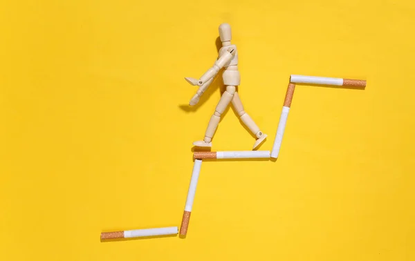 悪い習慣による社会的劣化 黄色の背景にタバコの階段を木製の人形ステップダウン — ストック写真