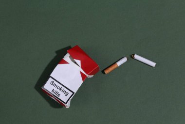 Sigarayı bırakıyorum. Yeşil arka planda buruşuk paket ve kırık sigara.