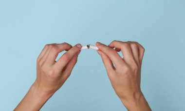 Kadın eli mavi arka planda sigara kırar. Sigarayı bırakmak