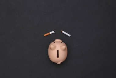 Siyah arka planda kırık sigara ve kumbara. Sigarayı bırakmak, para biriktirmek.