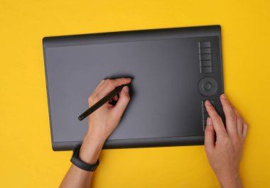 Kadın grafik tasarımcısı ya da rötuş uzmanı sarı arka planda grafik tabletle çalışıyor. Üst görünüm