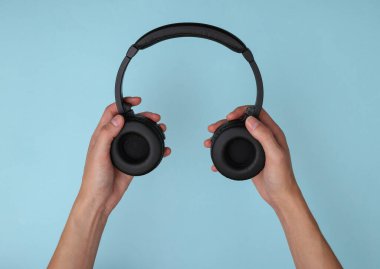 Mavi arka planda stereo kulaklık tutan eller