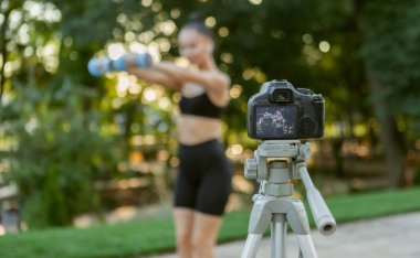 Çevrimiçi fitness eğitmeni. Çekici, formda genç bir kadın dambıllarla egzersiz yapmayı, sabahları dışarıda kamera önünde blog çekmeyi öğretiyor. Spor günlüğü, fitness vlog