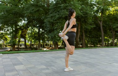 Spor kıyafetli genç bir kadın dışarıda koşmadan önce bacak esnetiyor.