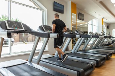 Yakışıklı kaslı erkek vücut geliştirici modern bir spor salonunda koşu bandında egzersiz yapıyor. Kardiyo çalışması
