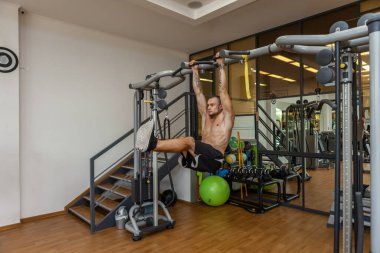 Genç kaslı fitness adamı spor salonundaki yatay çubukta sallanırken karın kaslarını çalıştırıyor.