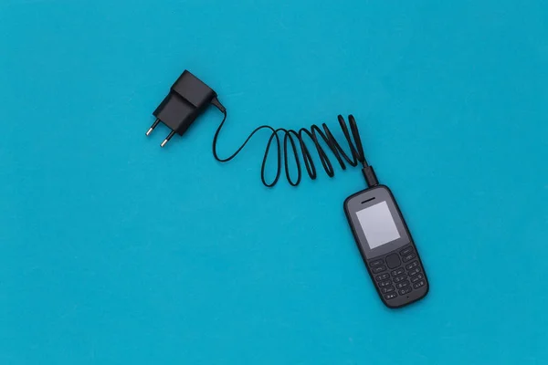 Push-button telephone with a charging adapter on a blue background. Top view