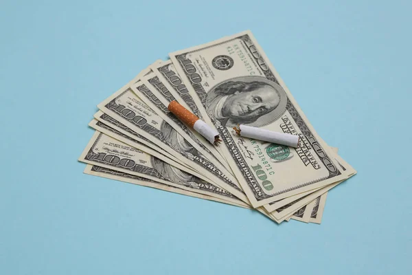 Broken cigarette with one hundred dollar bills on blue background