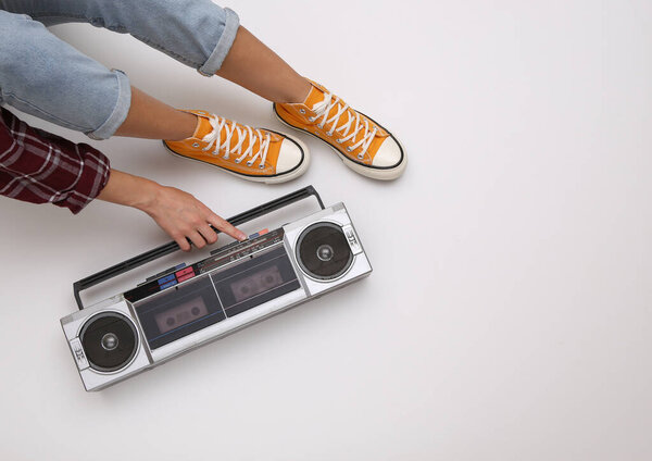 Woman in youth clothing retro 80s style turns on audio boombox tape recorder while sitting on white background