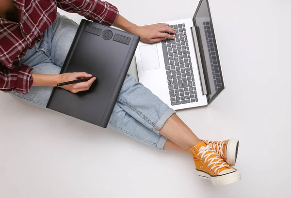 Graphic designer or photographer job. Woman works with graphic tablet and laptop while sitting on a white background. Freelance, online work concept. Top view