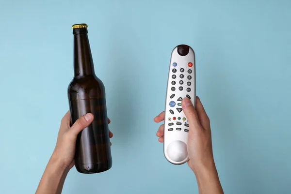 Χέρι Κρατήσει Ένα Μπουκάλι Μπύρα Και Τηλεχειριστήριο Τηλεόραση Μπλε Φόντο — Φωτογραφία Αρχείου