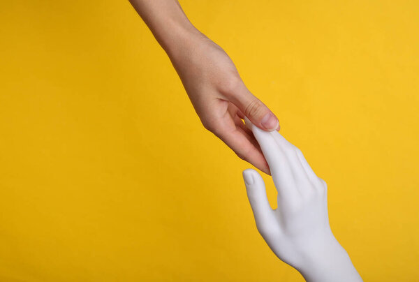 A human hand touches the hand of mannequin on yellow background. Artificial intelligence concept