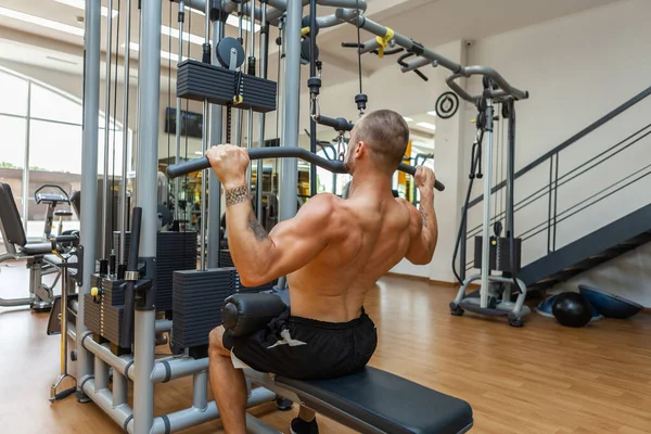 健身健美肌肉男 赤身裸体 在体操馆的拉力机上锻炼 — 图库照片