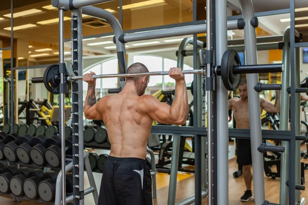 肌肉发达 体格强壮的男性健美运动员在体育馆里从后脑勺上按下了杠铃 背景色 — 图库照片