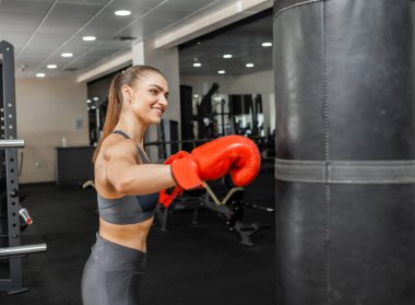 Formda kadın boksör trenleri spor salonunda kum torbasıyla yumruk atıyor.