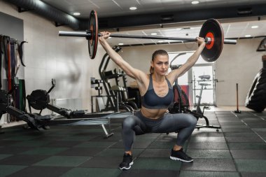 Spor giyim sektöründe atletik formda bir kadın modern spor salonunda ağır halterlerle antrenman yapıyor.