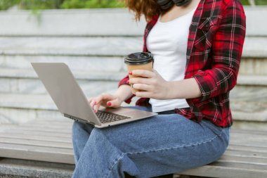 Laptop kullanan ve dışarıda kahve içen neşeli genç bir kız öğrenci. Mesafe çalışması veya eğitim kavramı