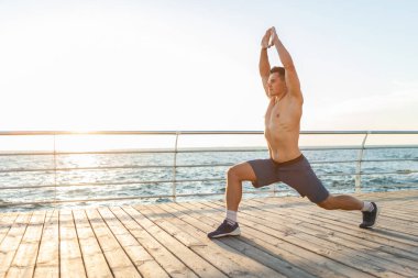 Çıplak gövdeli kaslı yakışıklı adam güneş doğarken Asana 'ya poz veriyor. Sağlıklı yaşam tarzı kavramı