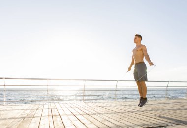 Güneş doğarken sahilde ip atlayan kaslı bir sporcu. Sağlıklı yaşam tarzı kavramı