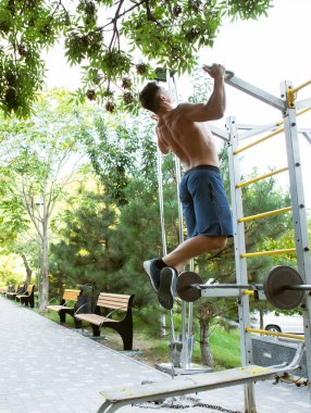Dışarıda spor yapan yakışıklı bir erkek sporcu. Adam kendini yatay çubuğa doğru çekiyor. Sağlıklı yaşam tarzı
