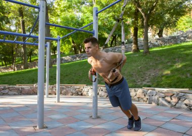 Açık hava spor sahasında trx direnç sistemi olan çıplak gövdeli genç bir adam. Sağlıklı yaşam tarzı kavramı