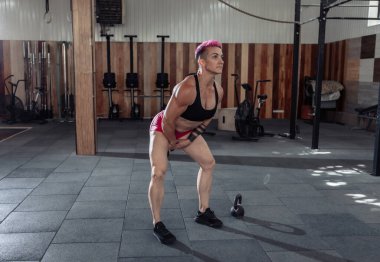 Kısa pembe saçlı, kaslı, olağanüstü bayan sporcu ağır kettlebell 'lerle sallanıyor. Modern spor salonunda işlevsel, çapraz eğitim.