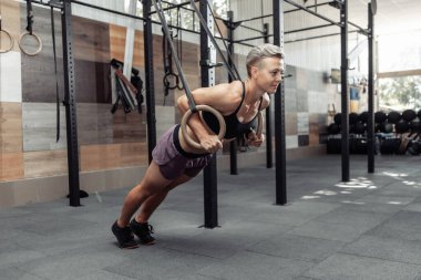 Modern çapraz spor salonunda jimnastik yüzükleriyle egzersiz yapan atletik bir kadın.